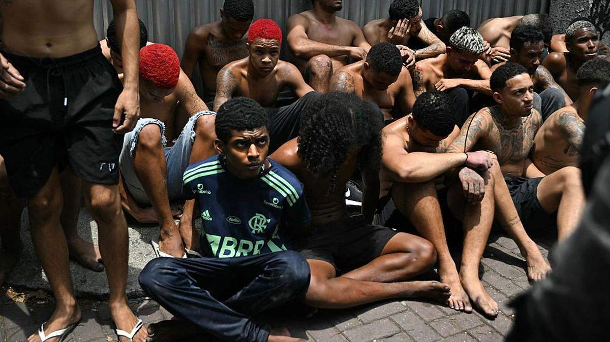 An alleged criminal arrested during the Operacao Contencao (Operation Containment) at the Vila Cruzeiro favela stares at a police officer, in the Penha complex, in Rio de Janeiro, Brazil, on October 28, 2025. At least 2,500 security forces agents took part in an operation to arrest drug traffickers from the Comando Vermelho (CV), which resulted in 64 people dead, authorities reported. (Photo by Mauro PIMENTEL / AFP) (Photo by MAURO PIMENTEL/AFP via Getty Images)
