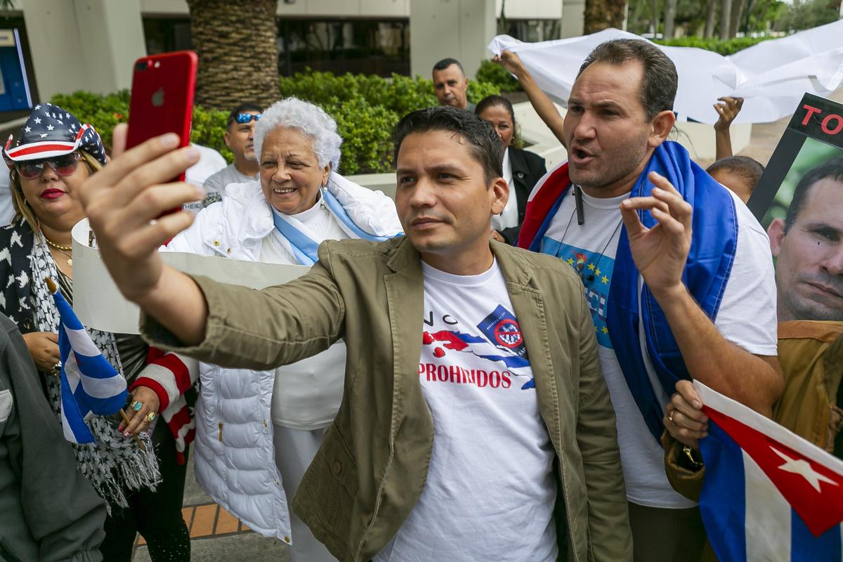 Eliécer Ávila, 34, en el centro, y Luis Enrique Ferrer, a la derecha, hacen una transmisión en vivo durante una protesta fuera del Consulado de España en Miami, Florida, el sábado 9 de noviembre de 2019.