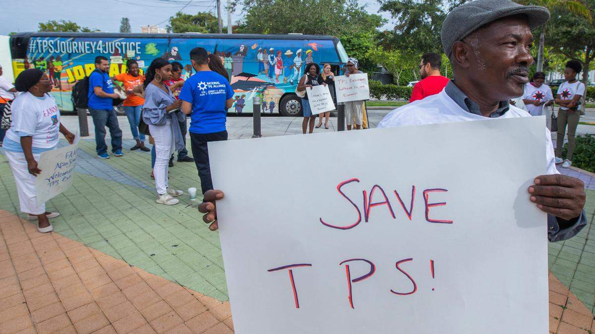 Michel Bien-Aime holds a sign “Save TPS” when a bus from Nation TPS Alliance arrives at the Little Haiti Cultural Center.