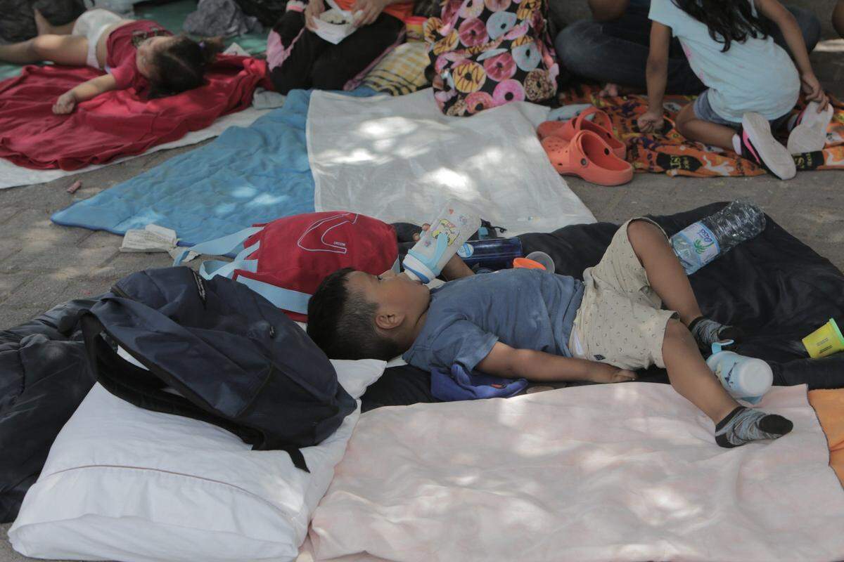 Un niño peruano bebe leche bajo la sombra de un árbol en el campamento ubicado en un pequeño parque junto a la entrada del Puente Internacional de Matamoros, México.