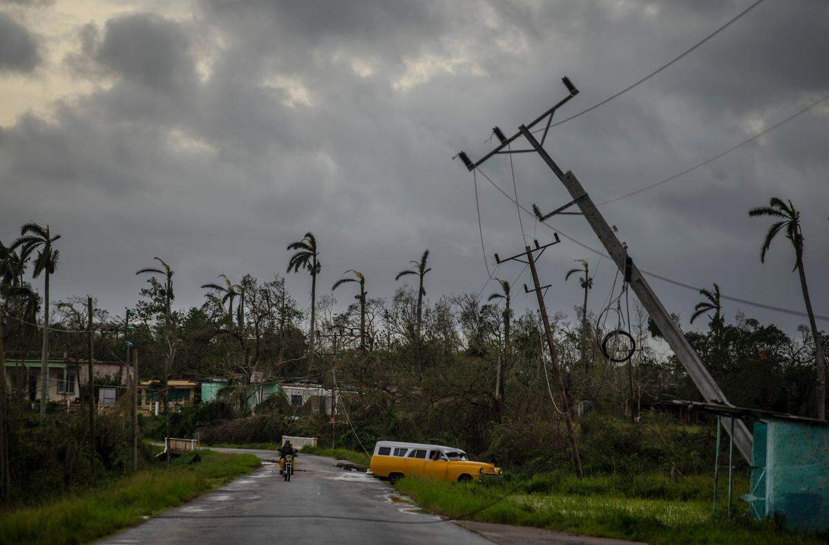 Un antiguo automóvil estadounidense pasa junto a los postes de electricidad inclinados por el huracán Ian en Pinar del Río, Cuba, el martes 27 de septiembre de 2022.