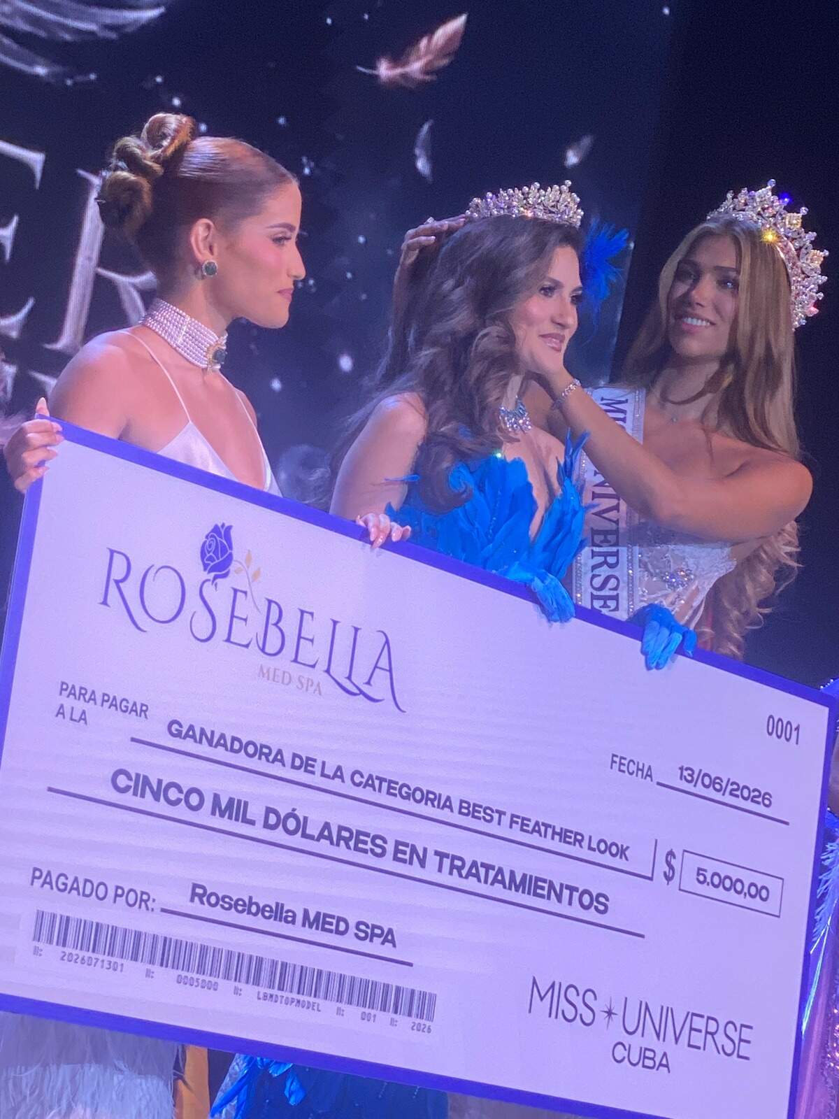 Leah Reyes Amores, Miss Teen Earth 2025 y jurado del desfile Feather Fantasy, entrega un cheque simbólico de $5,000 a Lizlauren Mosquera, ganadora del ‘Mejor look de plumas’, junto a Lina Luaces, Miss Universe Cuba 2025.