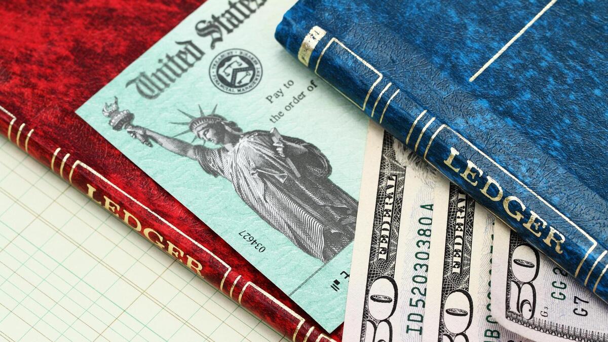 Un cheque de devolución de impuestos de el IRS y varios billetes de $50 aparecen entre dos libros contables.