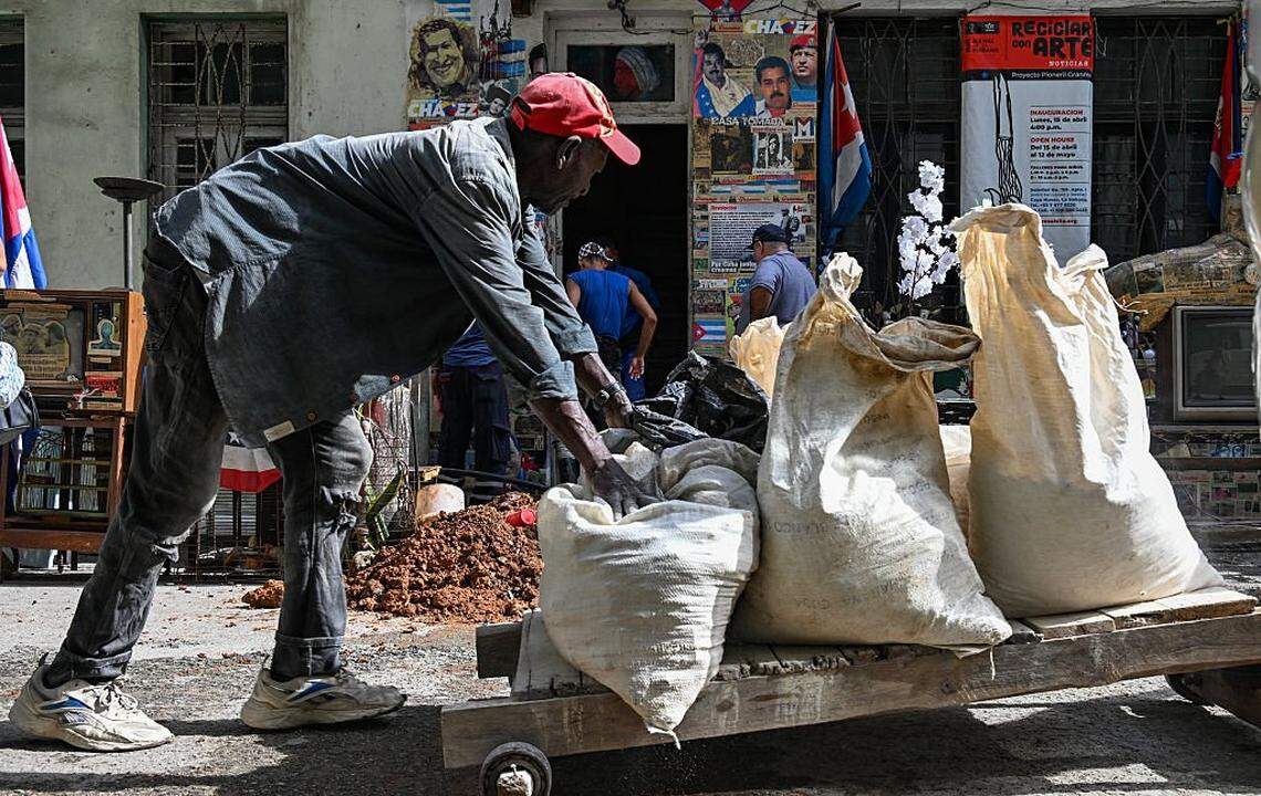 A man transports items near a house displaying a poster of deposed Venezuelan President Nicolas Maduro and the country's late leader Hugo Chavez in Havana on January 14, 2026. (Photo by YAMIL LAGE / AFP via Getty Images)