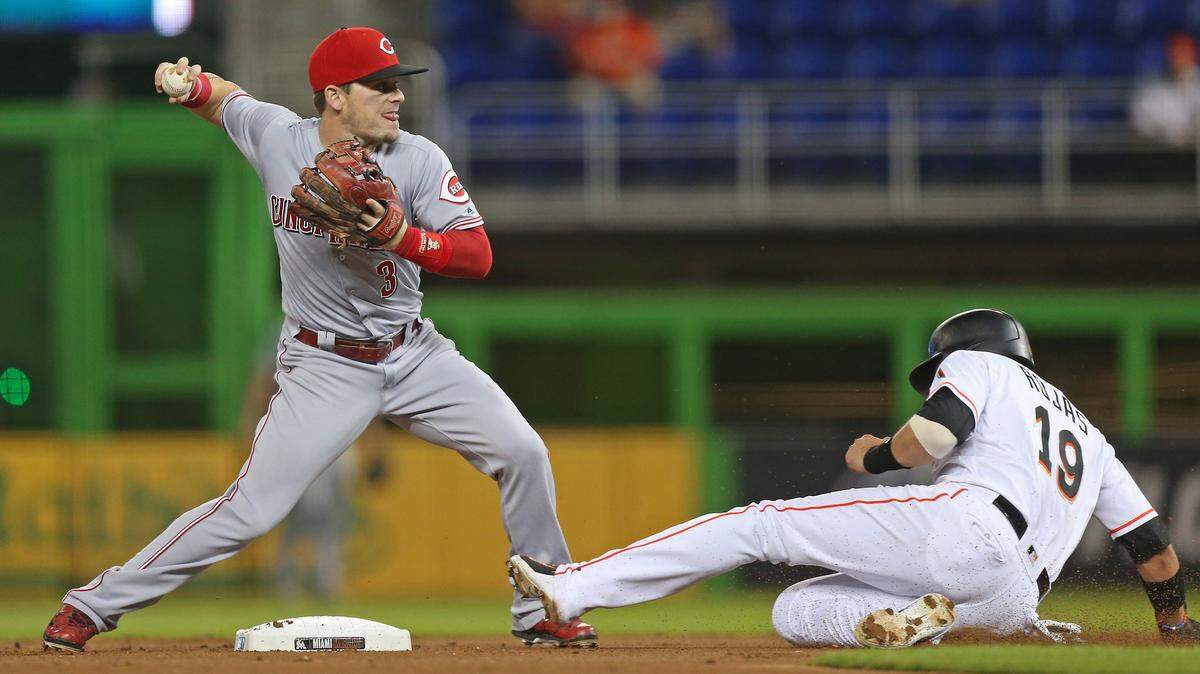 Miguel Rojas se desliza en segunda base en tanto Scooter Gennett, de los Rojos, tira a primera base en una jugada en el primer inning del partido celebrado el 20 de septiembre de 2018 en Miami.