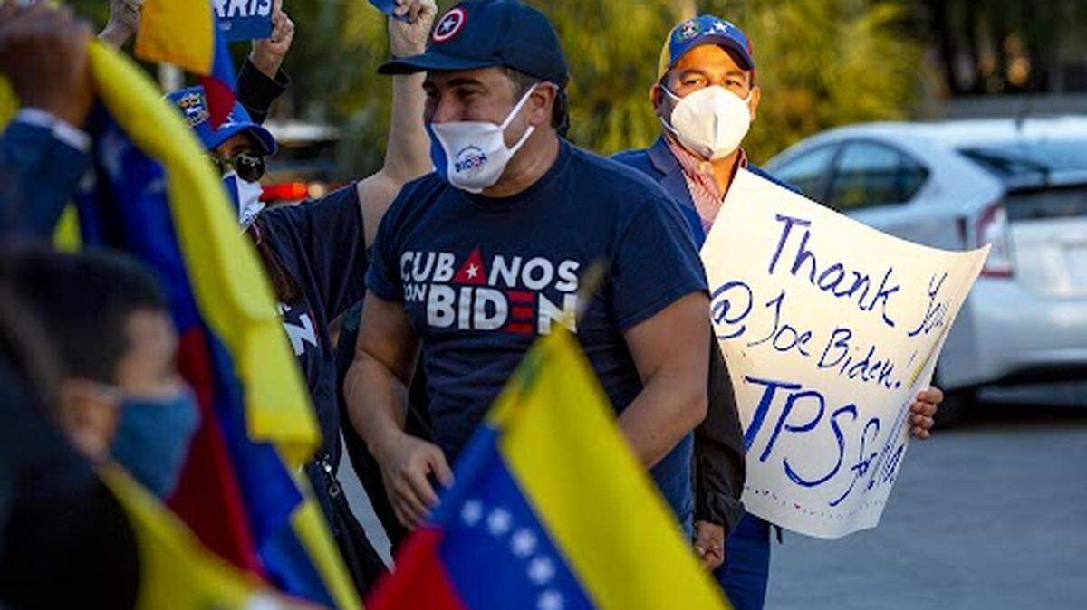 Personas ondean la bandera de Venezuela y sostienen carteles agradeciendo al presidente Joe Biden mientras celebran la aprobación del Estatus de Protección Temporal para más de 300,000 ciudadanos venezolanos que viven en Estados Unidos, en El Arepazo en Doral, Florida, el martes 9 de marzo de 2021.