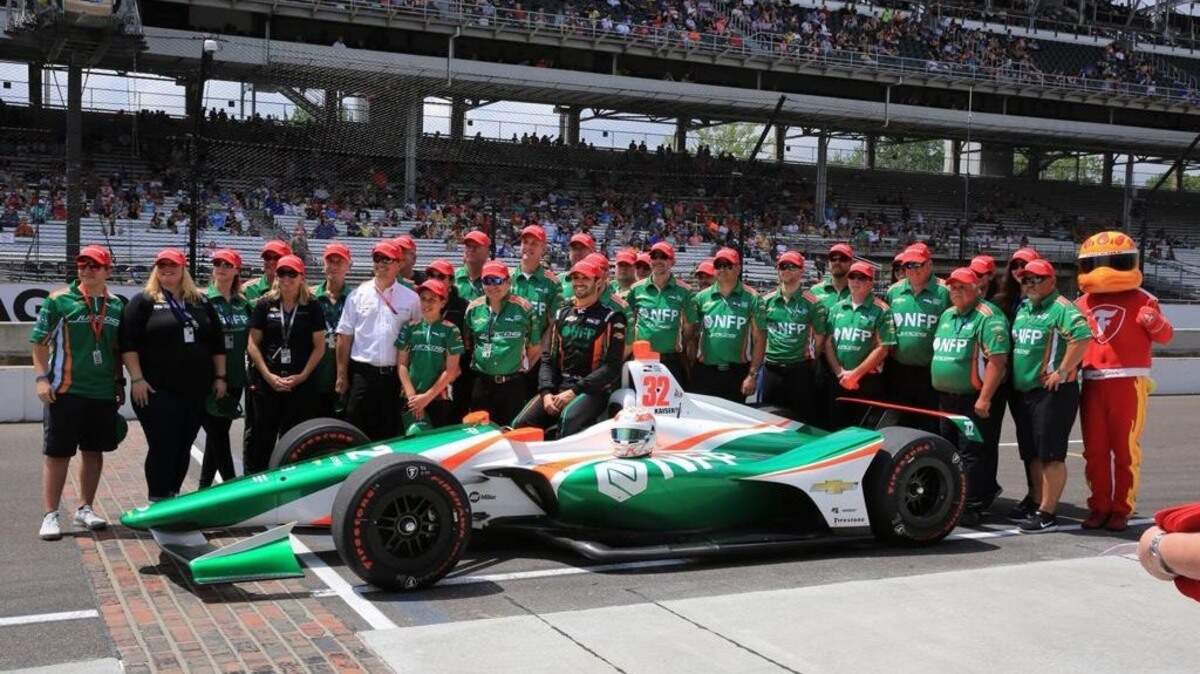 Ricando Juncos (camisa Blanca) posa con unos de los autos y miembros de su escudería Juncos Racing de la IndyCar.