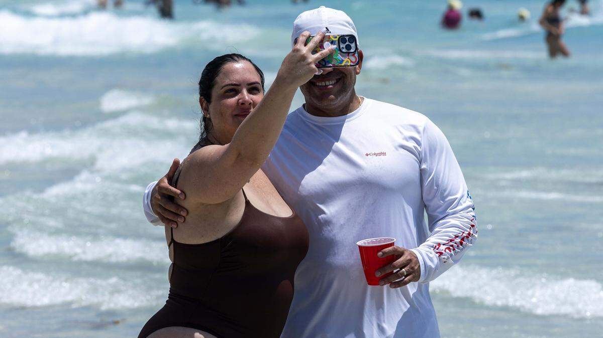 Un hombre y una mujer se toman una selfie entre las olas durante el Día de los Caídos en South Beach, el lunes 25 de mayo de 2025 en Miami Beach, Florida.