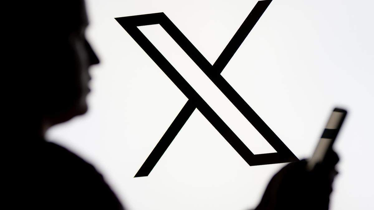 En esta ilustración fotográfica, se ve a una mujer mirando un teléfono inteligente con el logotipo de X (Twitter) mostrado en el fondo. 