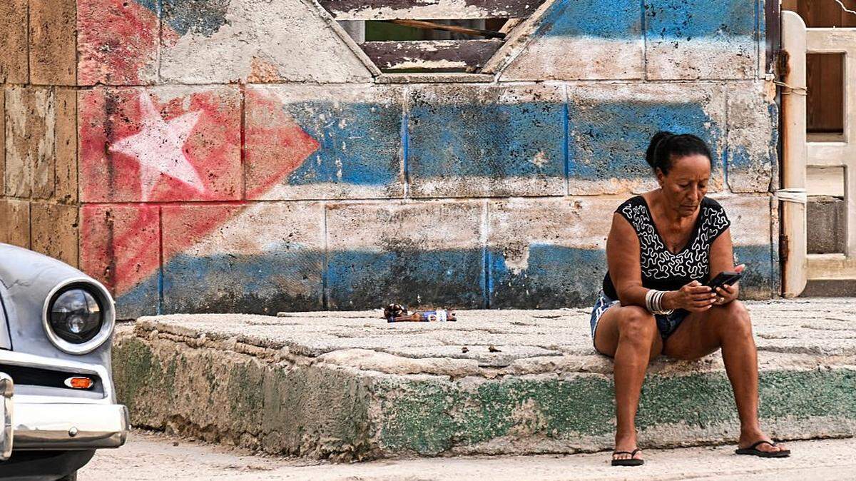 A woman looks at her cellphone on a street in Havana on February 23, 2026. Cuban Foreign Minister Bruno Rodriguez on February 23 accused the United States of trying to trigger a "humanitarian catastrophe" in his country with an oil blockade he called an "aggressive escalation". (Photo by YAMIL LAGE / AFP via Getty Images)