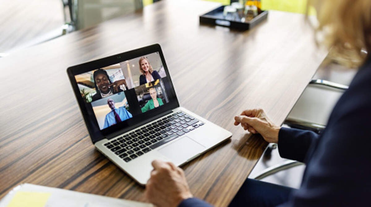 Over the shoulder view of a businesswoman having a video call with colleagues over the laptop. Multi-ethnic group of businesspeople seen on laptop screen having a video conference.