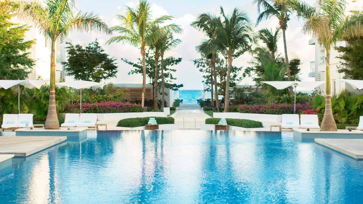 La piscina con sus islas con tumbadoras y camastros en madera opuestos al blanco edificio con cristal, pueden dar un aire muy South Beach.