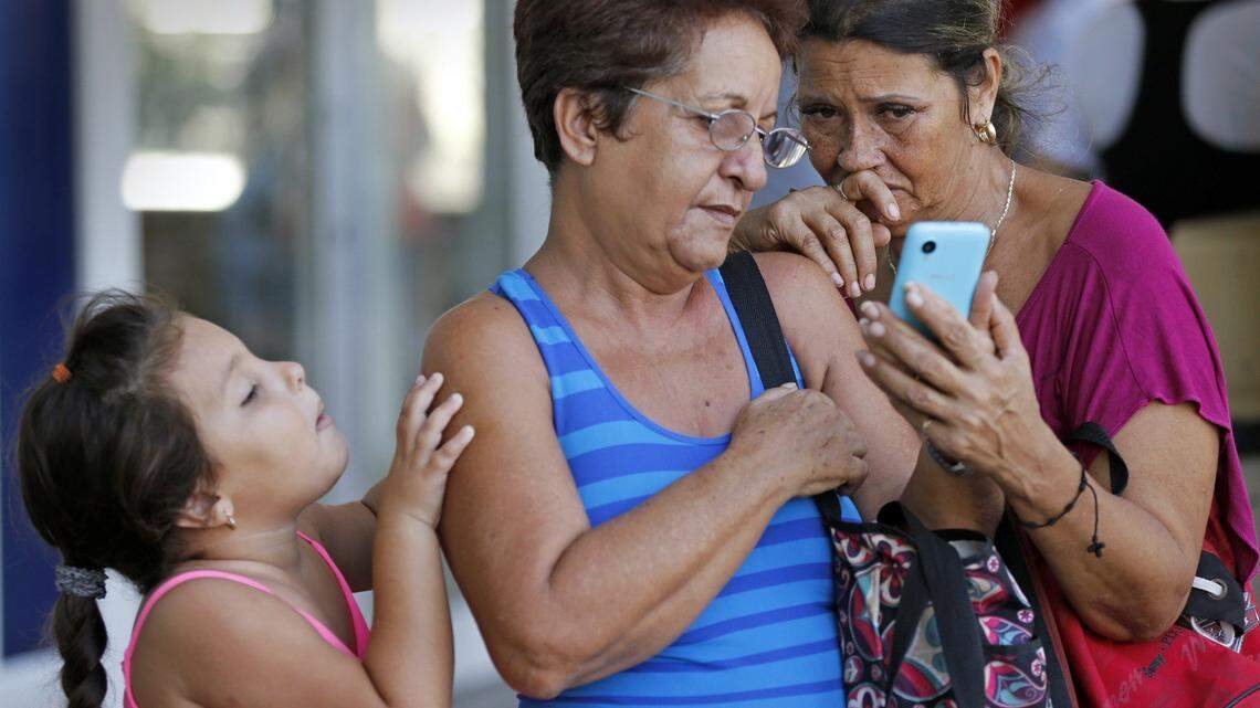 Clarita Moreno and Estel Mercedes Rodriguez speak with Rodriguez's son, who lives in Hungary, as a curious Angelina Arcia, 6, attempts to get a look at the cellphone in Havana, Cuba, on Sept. 19, 2015. Cubans are increasingly using the balance of their cellphone accounts with the government's ETECSA telecommunications monopoly as a virtual currency sometimes called "el ETECSO."