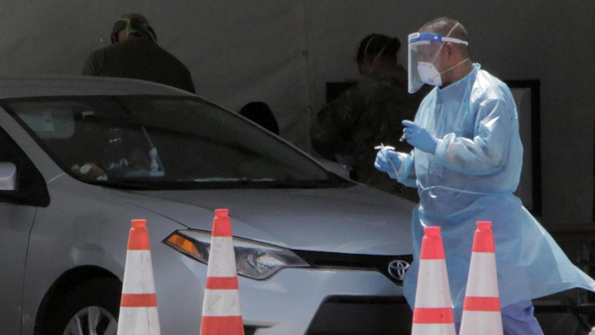Miami Gardens, Florida, July 16, 2020- A nurse walks around the passenger side of a vehicle ready to administer a Covid-19 test at the Hard Rock stadium site in Miami Gardens, Florida