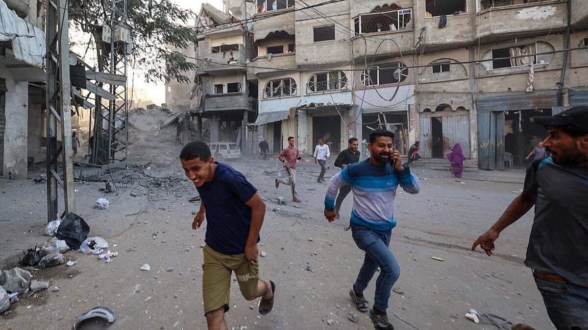 TOPSHOT - People run for cover following an Israeli strike that targeted a building in the Bureij camp for Palestinian refugees in the central Gaza Strip on October 19, 2025. Gaza's civil defence agency said a series of Israeli air strikes on October 19 killed at least 11 people across the territory, as Israel and Hamas traded blame for violating a ceasefire. (Photo by Eyad BABA / AFP) (Photo by EYAD BABA/AFP via Getty Images)
