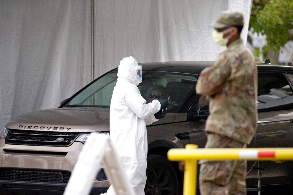 A Florida Army National Guard looks on as a healthcare worker holds a swab tests from citizens at the COVID-19 drive-thru testing center at Marlins Park as the coronavirus pandemic continues on Wednesday, March 25, 2020 in Miami.