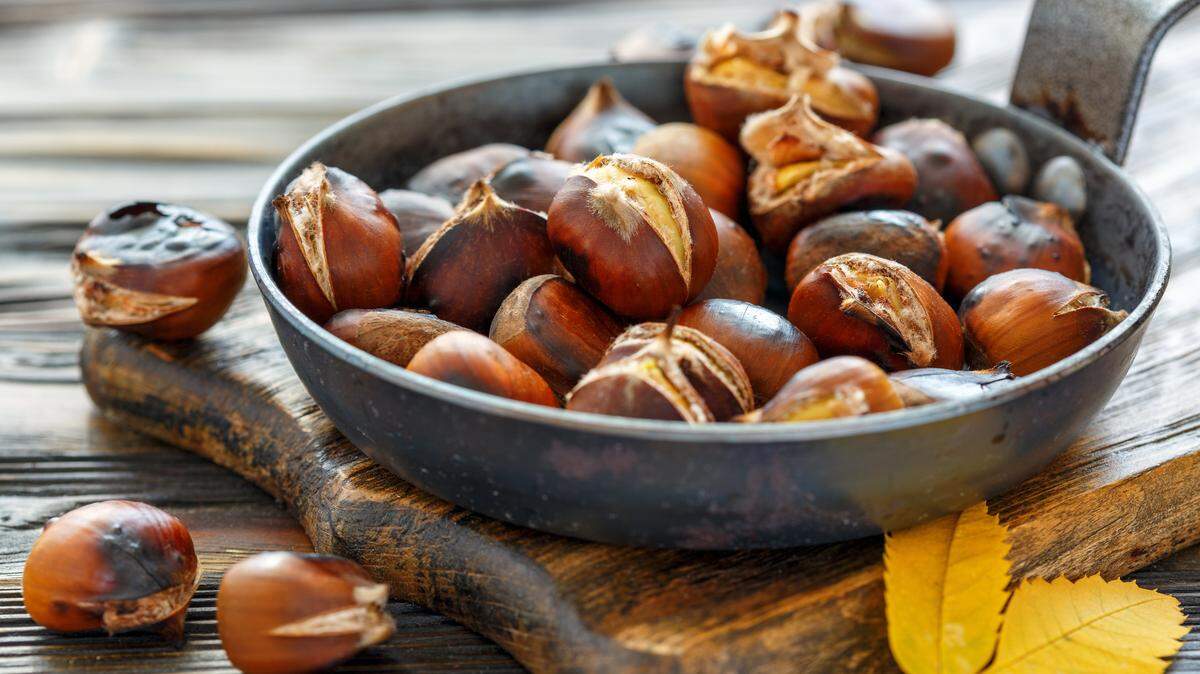 Cast iron skillet roasted chestnuts on the old wooden table, selective focus.