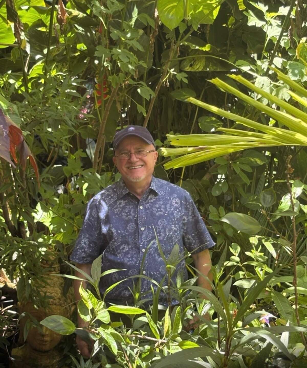 El artista, en el patio trasero de su casa, entre ramas, troncos y arbustos, entre flores y hojas de distintas formas y tamaños.