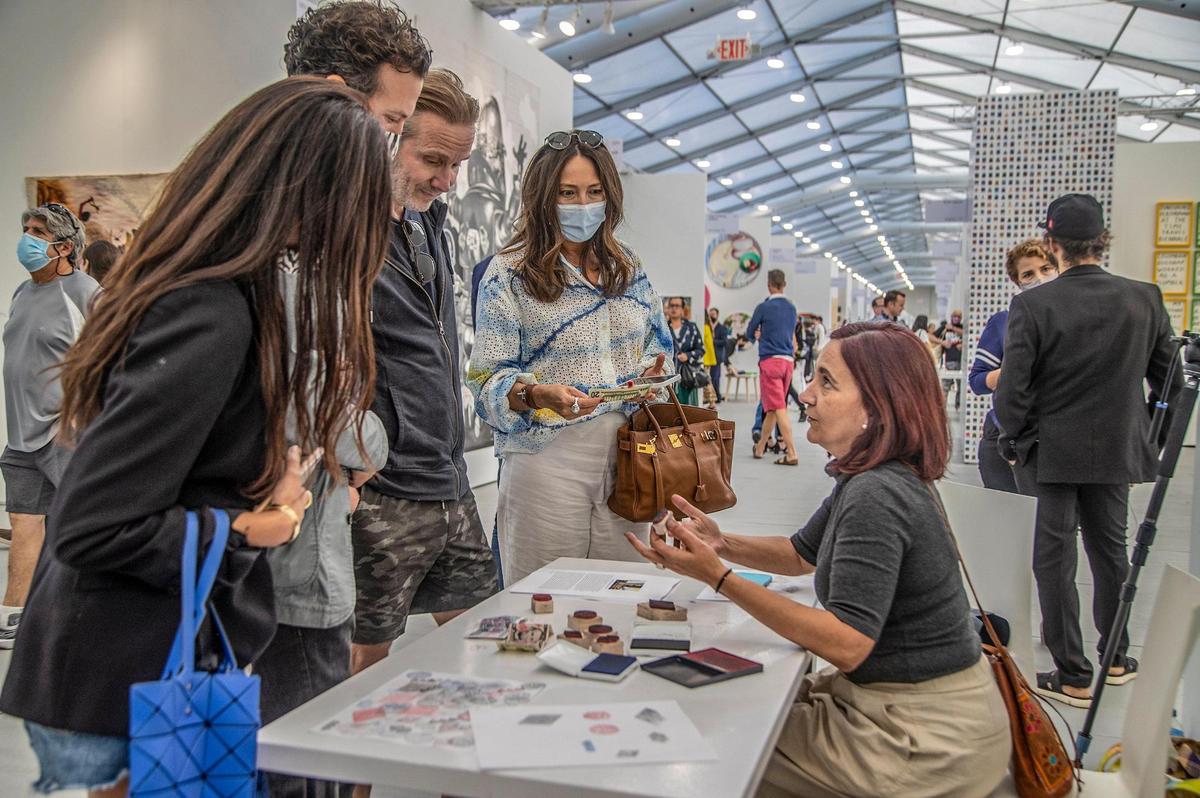 La curadora Janet Batet estampa billete y explica al público los cuños en el ‘performance’ de Hamlet Lavastida, “El billetaje quemando la calle/Bills Burning the Street”, en Untitled Art Fair, en Miami Beach, el 29 de noviembre.