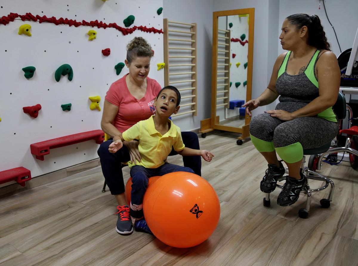 Brenda López talks to physical therapist Ana Lebrón as her son Angel Torres practices sitting at the Centro Ayani clinic in Puerto Rico. Angel has cerebral palsy and is learning to stand on his own.