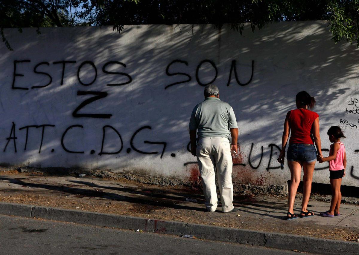 Residentes examinan manchas de sangre y grafitis en la escena del crimen en Monterrey, México, el 15 de junio de 2011. Los asesinos mataron a tres personas en la escena, dejando un mensaje que decía: “Estos son Z, amablemente CDG”, lo que significa que eran miembros del cartel del Golfo que habían asesinado a Zetas.