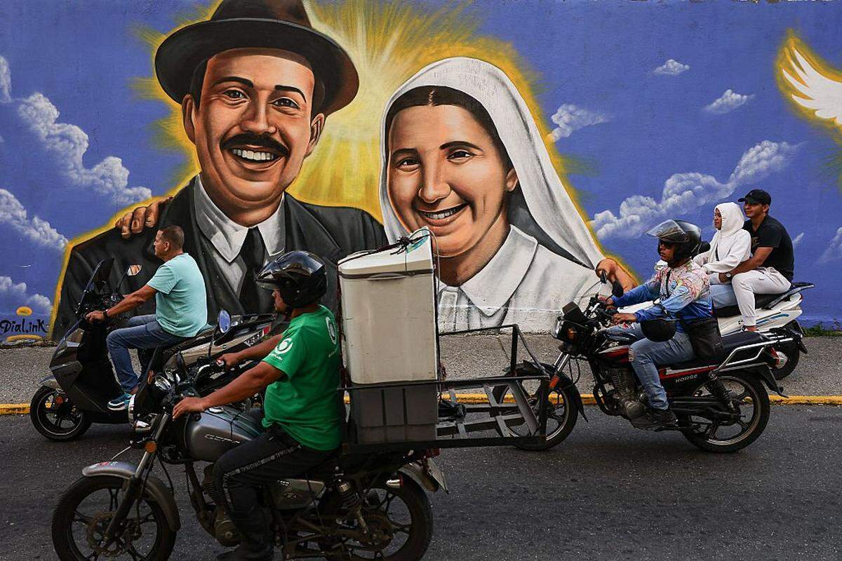 CARACAS, VENEZUELA - OCTOBER 18: Motorcyclists ride in front of a mural painted in honor of the canonization of Blessed JosÃ© Gregorio HernÃ(degrees)ndez and Blessed Carmen Rendiles MartÃnez on October 18, 2025 in Caracas, Venezuela. Mother Carmen and JosÃ© Gregorio HernÃ(degrees)ndez Cisneros, a doctor, scientist, known as the "Doctor of the Poor" will be canonized by Pope Leo XIV during a solemn Mass at St. Peter's Basilica on October 19, 2025, and will be Venezuela's first two saints. (Photo by Jesus Vargas/Getty Images)