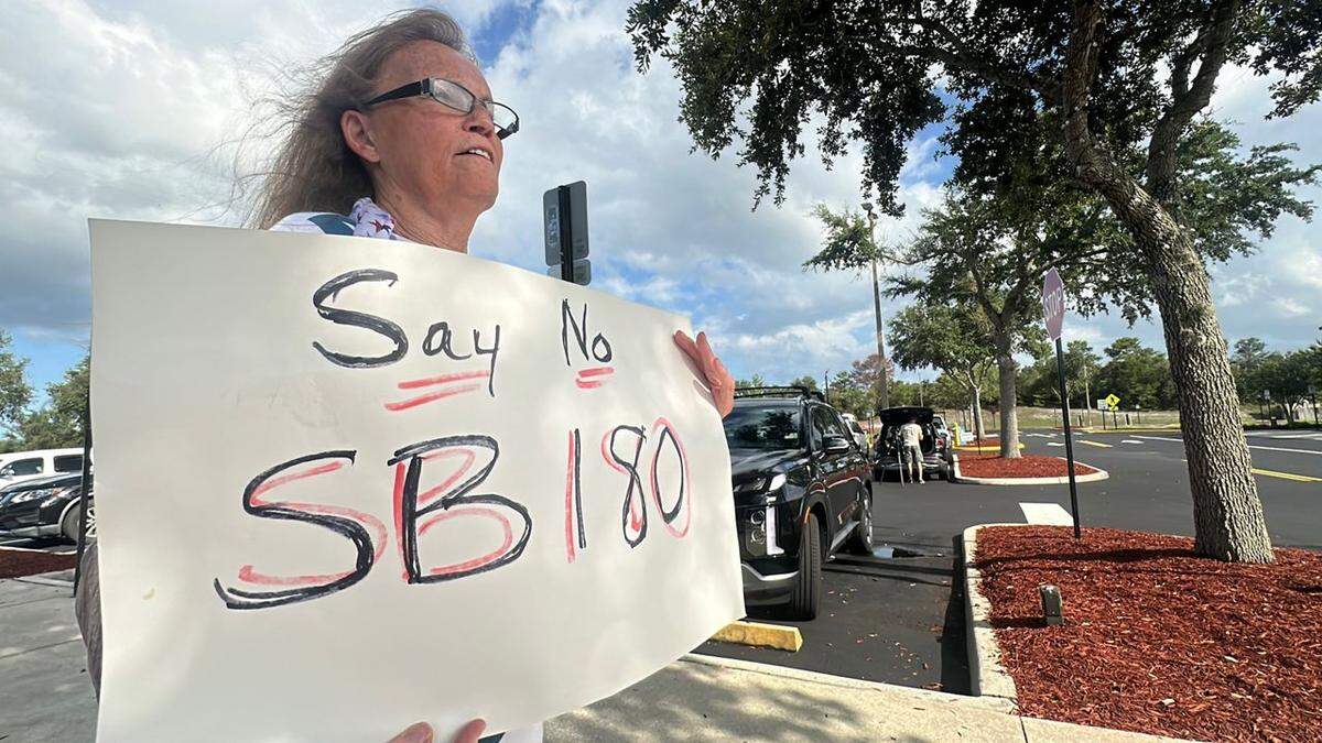 Stephanie Cox, residente de Deltona, Florida, sostiene un cartel que dice “Dígale No a la SB 180” antes de una reunión de la Comisión Municipal de Deltona en junio, donde los funcionarios aprobaron una moratoria al desarrollo residencial, desafiando la nueva ley estatal. Deltona es una de las ciudades que se unió a una demanda contra la SB 180.