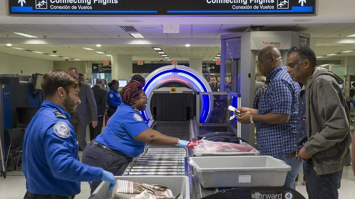 Agentes de la Administración de Seguridad del Transporte (TSA) ayudan a los pasajeros a colocar sus maletas a través de un escáner en el Aeropuerto Internacional de Miami.