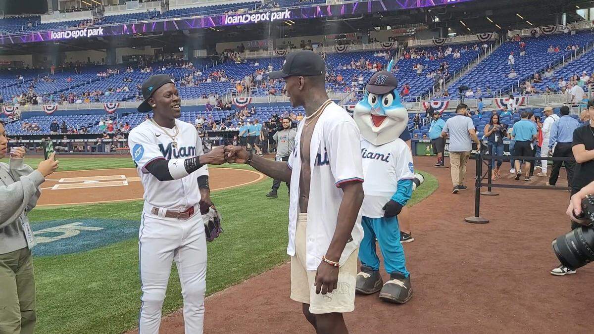 El jardinero Jazz Chisholm (izq.) saluda a Israel Adesanya luego de que el excampeón lanzara la primera bola en un juego de los Marlins.