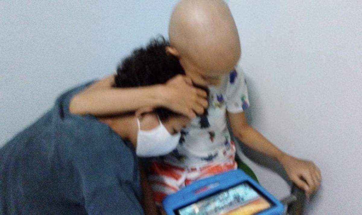 José Camilo Cateura Díaz abraza a su hermano Jean Manuel Cateura Díaz mientras ven un video en una tableta electrónica.