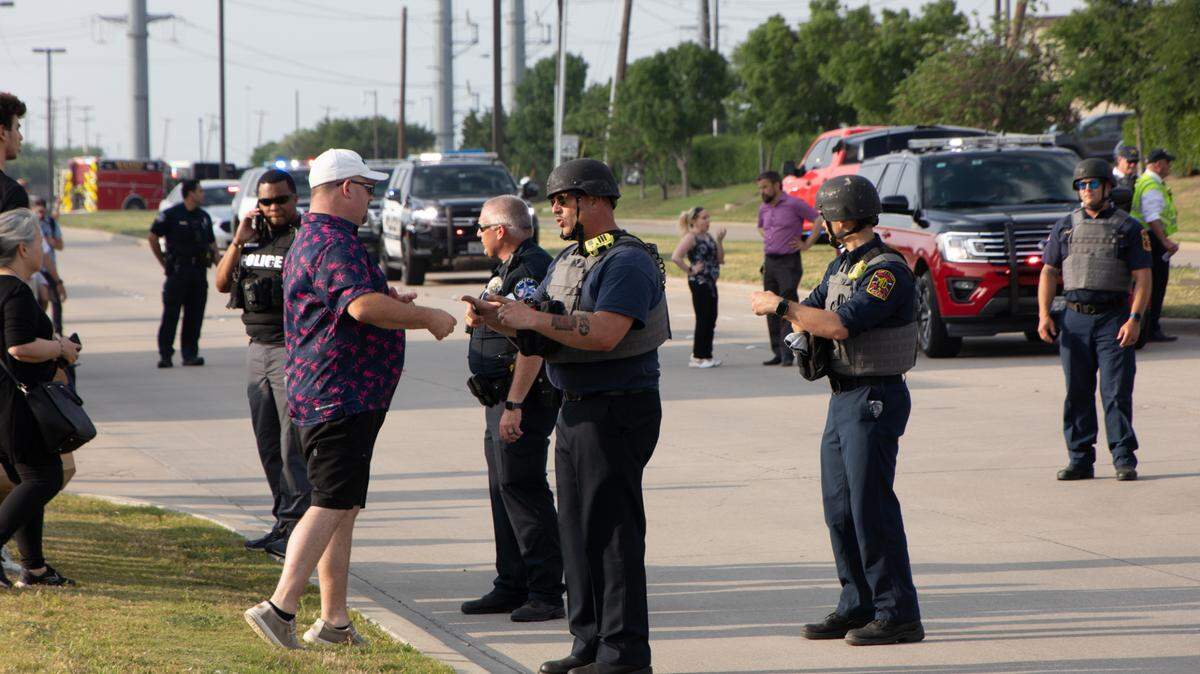 Un oficial de policía habla con un testigo cerca del sitio del tiroteo en Allen Premium Outlets en Dallas, Texas, el 6 de mayo de 2023. Nueve personas murieron, incluido el tirador, y otras siete resultaron heridas.