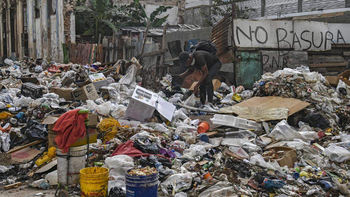 A man throws rubbish on a street in Havana on February 23, 2026, next to a wall reading "No rubbish". Many elderly people are forced to search through garbage to survive in Cuba, where the government does not collect the waste, which blocks passage in the streets.
