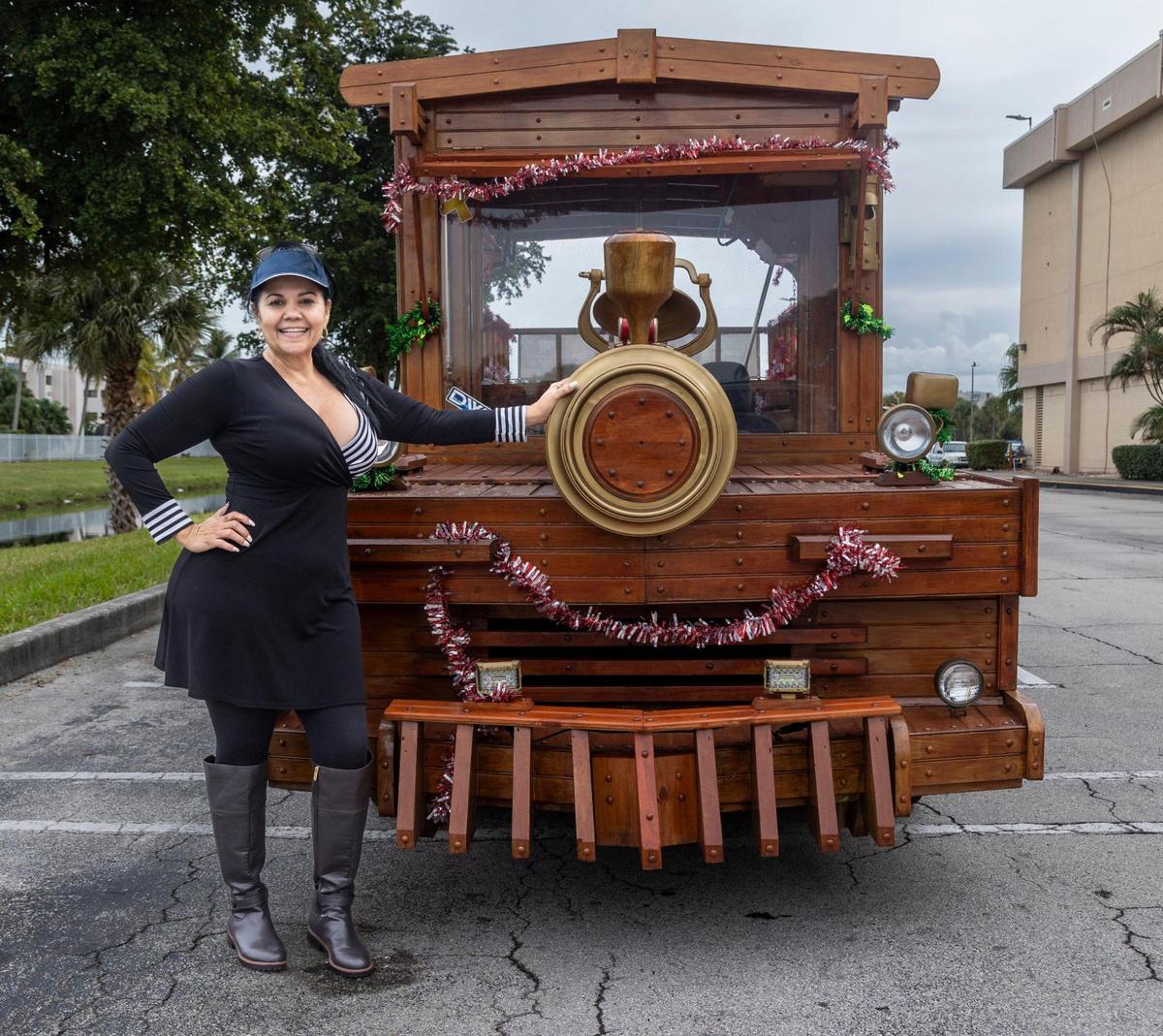 Xiomara Yani Pérez, propietaria del vehículo de madera junto con su esposo, posa junto al tren de madera, un vagón convertido para que parezca un tren, en el estacionamiento del Westland Mall en Hialeah. El vehículo se alquila para eventos, políticos o cualquier persona que busque un viaje único. Hialeah, Florida, 22 de diciembre de 2023 -