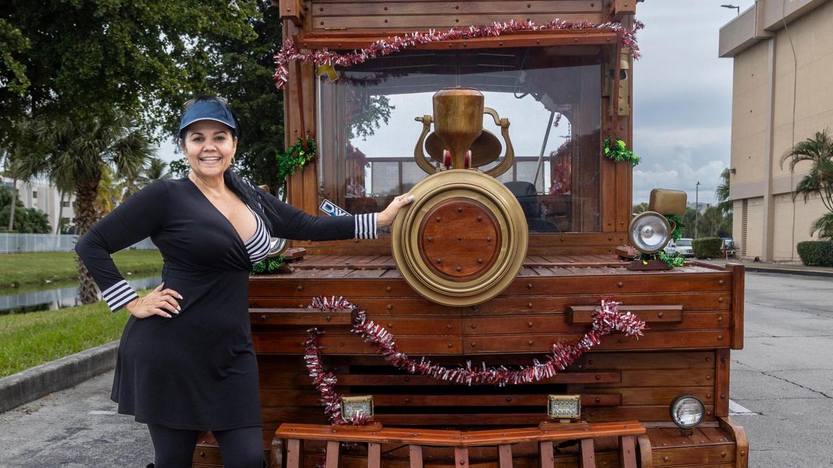 Xiomara Yani Pérez, propietaria del vehículo de madera junto con su esposo, posa junto al tren de madera, un vagón convertido para que parezca un tren, en el estacionamiento del Westland Mall en Hialeah. El vehículo se alquila para eventos, políticos o cualquier persona que busque un viaje único. Hialeah, Florida, 22 de diciembre de 2023 -