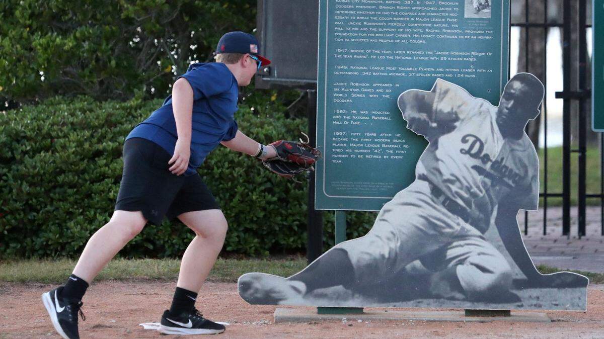 Un joven fanático del béisbol se inclina como si estuviera poniendo out a Jackie Robinson en la entrada del estadio de Daytona Beach, Florida, el 12 de abril de 2024.