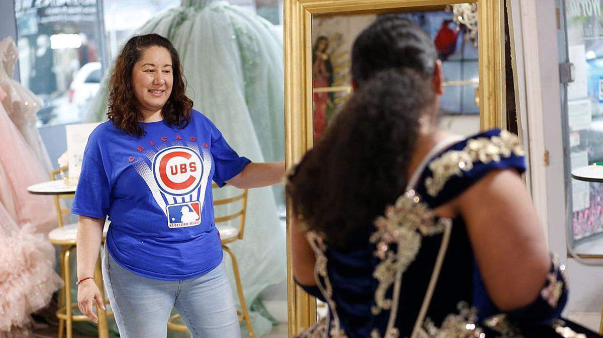 Ariella Santoyo (L), 38, the owner of 'My Quince World' in Chicago's Little Village, helps a teenager try on her dress for her upcoming quinceaÃ±era on October 11, 2025. The quinceanera dress shops in Chicago's Little Village neighborhood are usually bustling enterprises, reflecting the buoyant mood of Latino families looking to a brighter future. Not any more. Businesses across the city's immigrant-heavy districts are in peril, thanks to a crackdown by President Donald Trump's administration that is rippling fear across communities and sending immigrants indoors and out of view -- regardless of their immigration status. At the heart of Little Village, nicknamed the Mexico of the Midwest for its vibrant Mexican-American culture, streets were eerily empty Friday night -- when the hub is usually thumping with energy. (Photo by OCTAVIO JONES / AFP) (Photo by OCTAVIO JONES/AFP via Getty Images)          