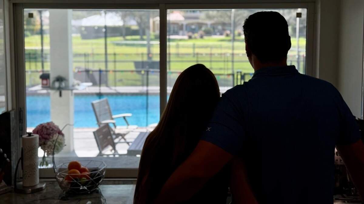 Michelle y Sean, cuyos nombres no son reales, están de pie junto a una ventana de su hogar en el sur de Florida. A Michelle se le concedió una visa H-1B mientras la pareja tramita la ciudadanía estadounidense.