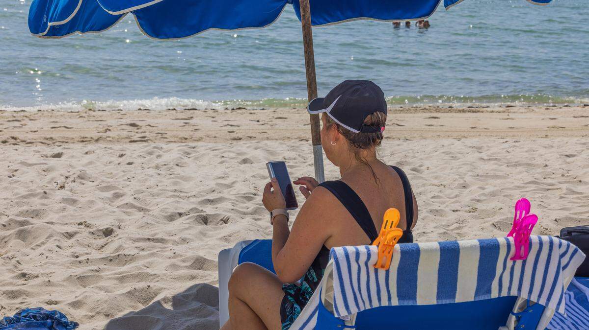 Una mujer sentada en una tumbona mira su teléfono móvil en Miami Beach. Archivo