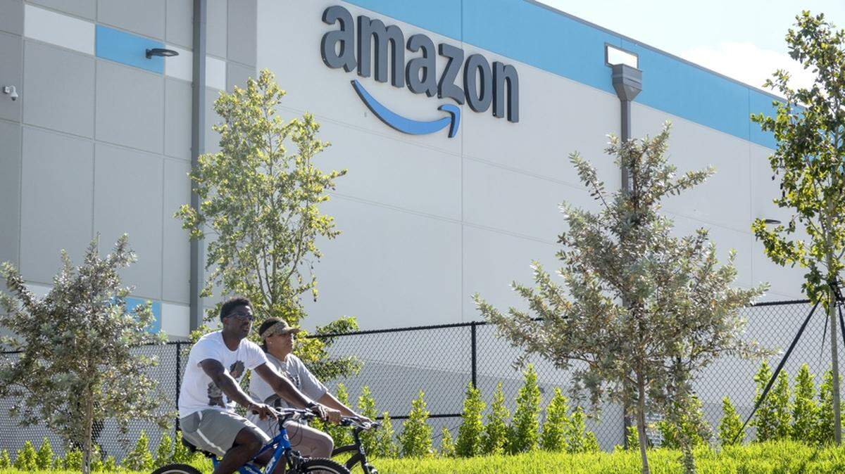 Fotografía de archivo de dos personas circulando en bicicleta frente a un centro logístico de Amazon en Florida (EE.UU.). Zoox, la empresa de vehículos autónomos propiedad de Amazon, inauguró una planta que se centrará en la producción de robotaxis en California, con la que busca hacer competencia a Waymo, según apuntan este miércoles los medios locales. EFE/EPA/ CRISTOBAL HERRERA-ULASHKEVICH / ARCHIVO