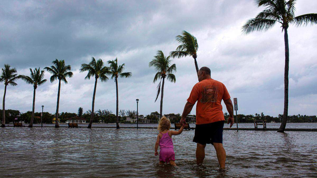 Un hombre camina con su nieta en un estacionamiento inundado en Lantana, Florida, el 3 de septiembre de 2019, en la víspera de la llegada del huracán Dorian.