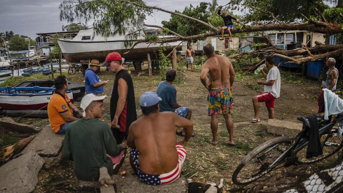 Residents watch as a person chops down a tree that fell on top of a boat due to Hurricane Ian in Havana, Cuba, Wednesday, Sept. 28, 2022. AP Photo/Ramon Espinosa