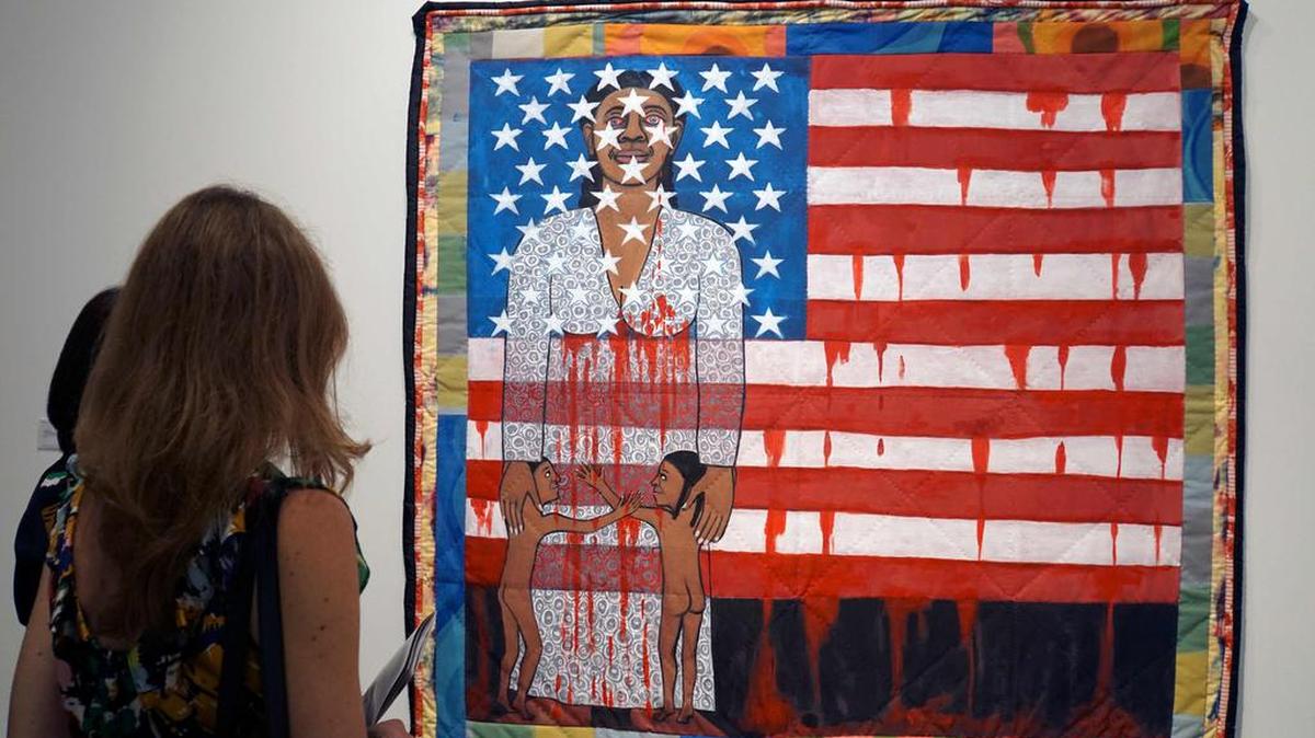 A visitor looks at the work of American artist Faith Ringgold, “The Flag is Bleeding 2” (1997), during a preview on December 4, 2019, before opening day of the annual Art Basel International Fair in Miami Beach in the first week of December.