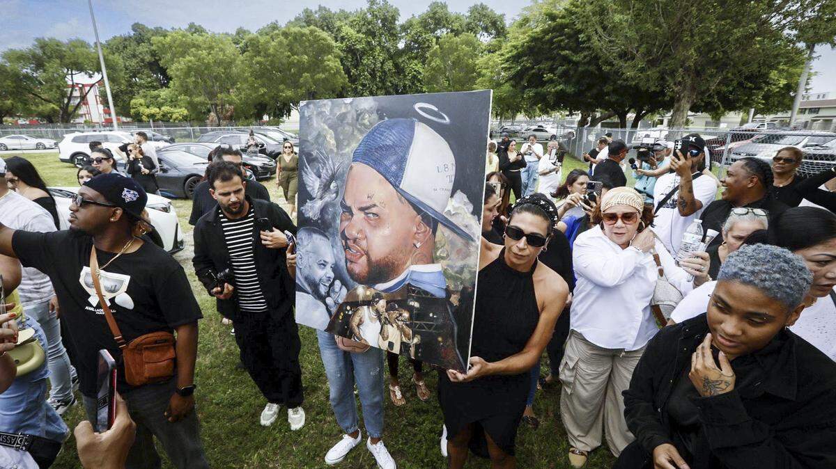 Emili Muñiz holds a portrait of El Taiger as people gather to mourn outside San Lazaro Catholic Church in Hialeah, after a funeral mass to honor the singer.
