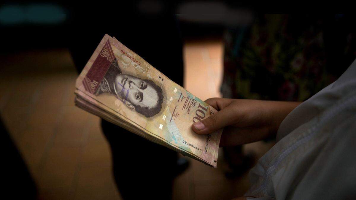 Un cliente sostiene una pila de billetes de 100 bolívares en una panadería en el centro de Caracas, Venezuela. Foto de archivo. 