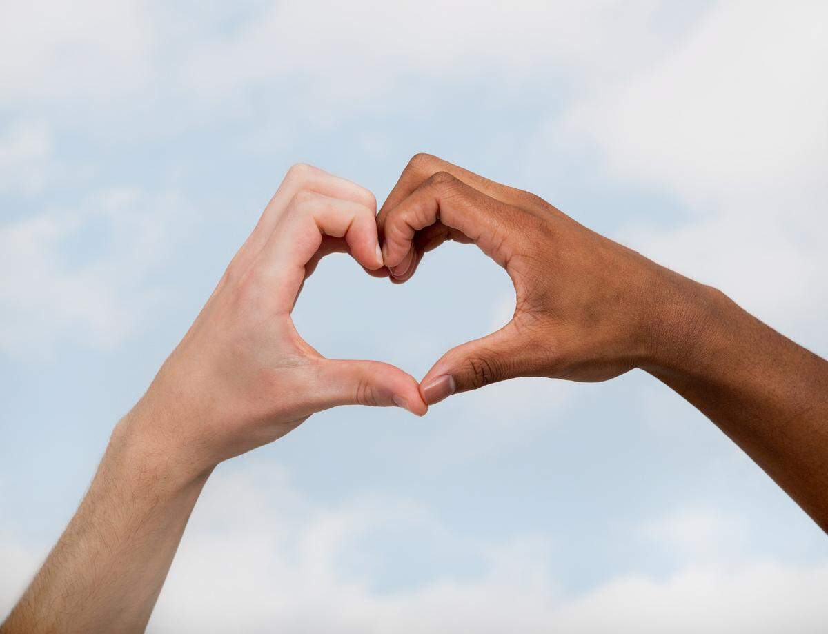 Two friends making a heart shape against a sky background
