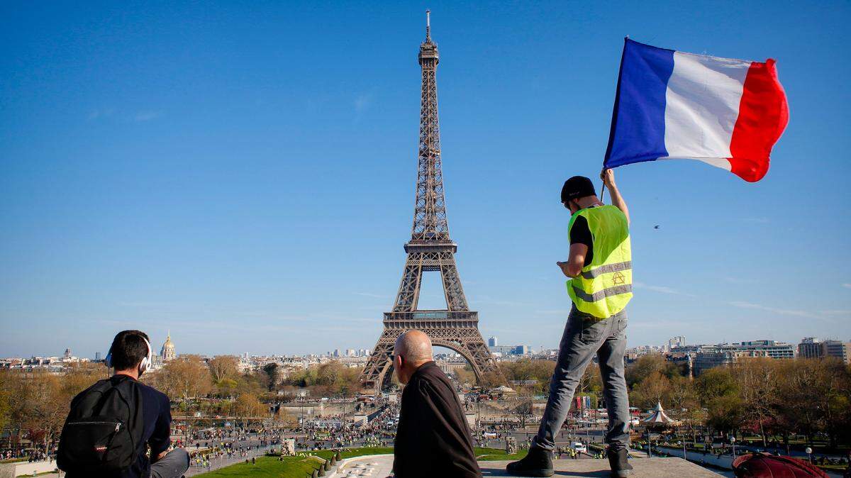 A man holds a French flag as French yellow vest protesters, backdropped by the Eiffel Tower are rallying to support an older woman activist injured in a confrontation with police, Saturday, March 30, 2019, in Paris. The demonstrators are undeterred by protest bans or repeated injuries in 20 weeks of demonstrations, marching again Saturday in Paris, Bordeaux and other cities to keep pressing President Emmanuel Macron to do more to help working classes, redesign French politics _ or step down altogether.