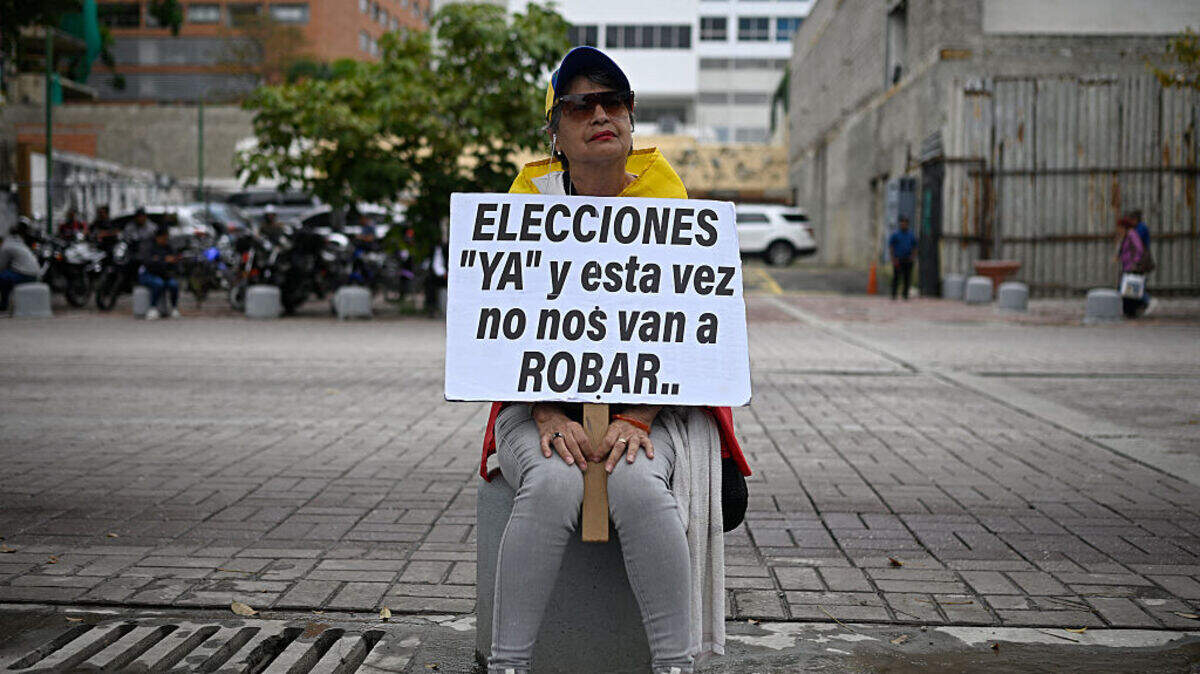 Una mujer envuelta en una bandera de Venezuela sostiene un cartel durante una protesta para exigir una transición política en el país, el 16 de abril de 2026 en la plaza Alfredo Sadel, en Caracas. 