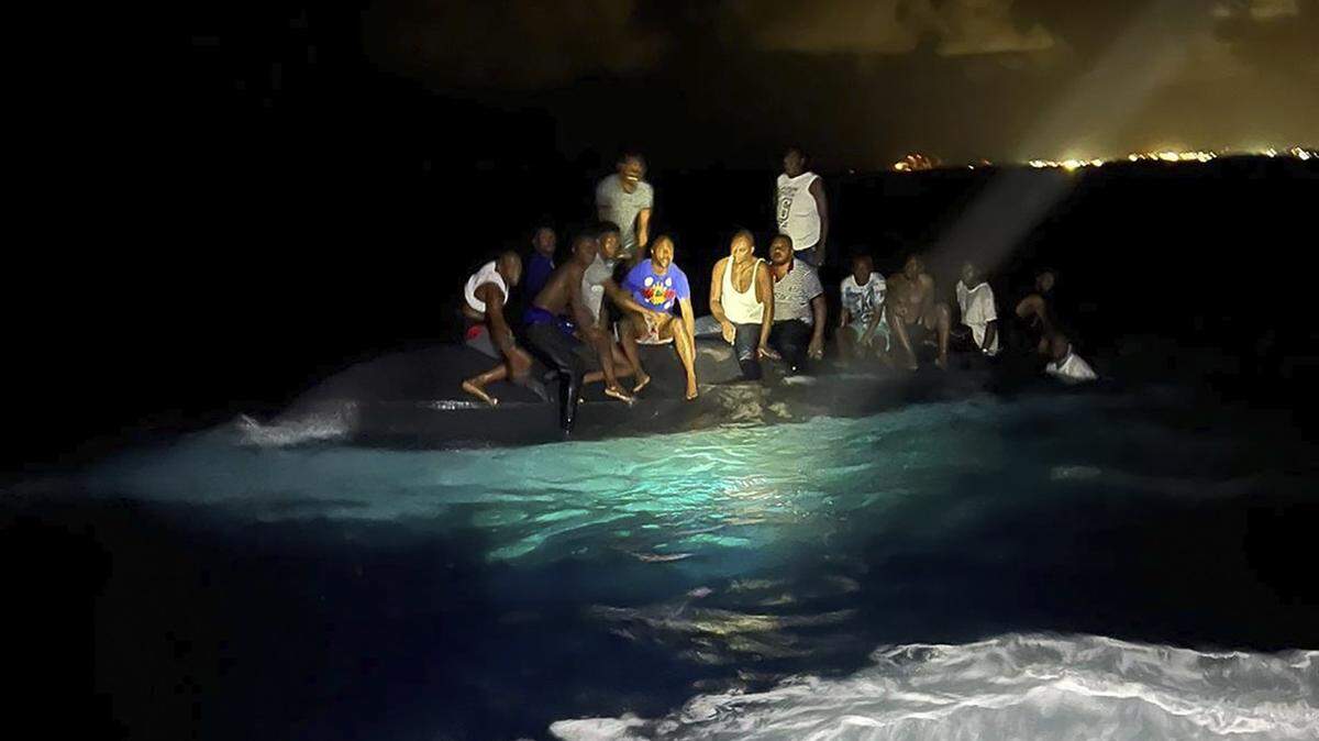 In this photo provided by the Royal Bahamas Defense Force, survivors sit on a capsized boat as they are about to be rescued near New Providence in the Bahamas, early Sunday. (Royal Bahamas Defense Force via AP)