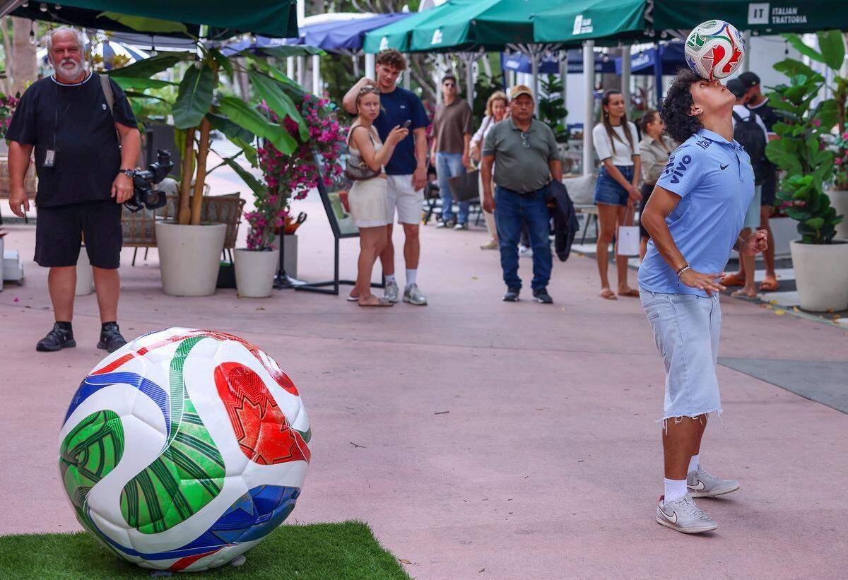 Ricky Martínez, de 22 años y jugador de fútbol de la Universidad St. Thomas, mantiene una pelota de fútbol en equilibrio sobre su cabeza mientras él y otras personas esperan para entrar a la nueva tienda de la Copa Mundial de la FIFA el lunes en Miami Beach.