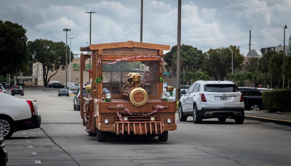El tren de madera avanza dentro del estacionamiento del Westland Mall en Hialeah, una ingeniosa idea de Julio Ramírez, un uruguayo que junto a su amigo Antonio Rodríguez, “maestro carpintero” acondicionaron un vehículo en un tren de madera. La esposa de Ramírez, Xiomara Pérez, es la conductora designada y su principal promotora. El tren se alquila para todo tipo de eventos, desde bautizos hasta divorcios. Hialeah, Florida, 22 de diciembre de 2023 -